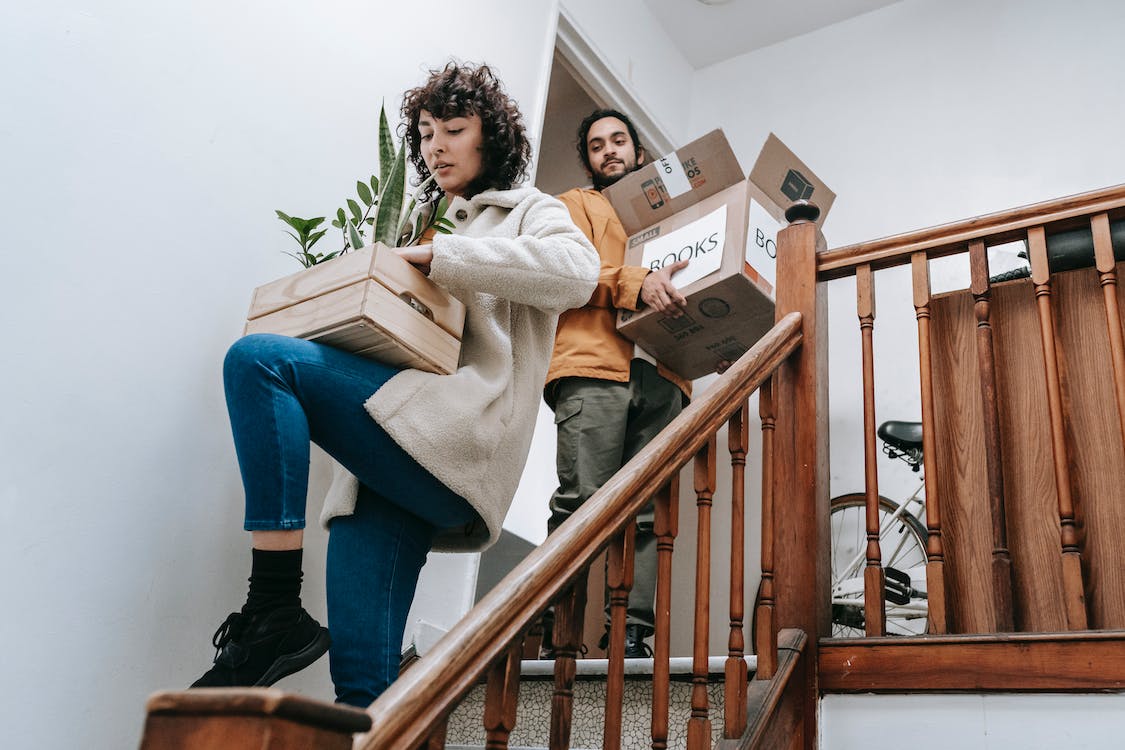 A couple carrying their moving boxes down the stairs