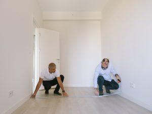 Two guys measuring the floor dimensions. 