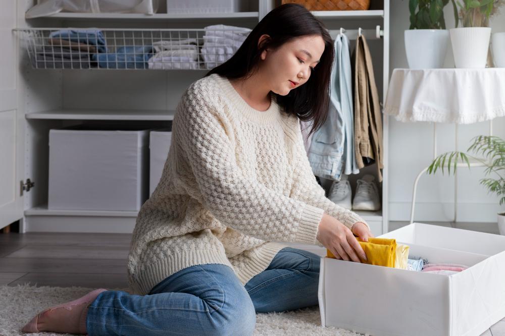 Woman in cream knitted sweater organizing clothes in a modern white wardrobe, exemplifying a tidy and cozy winter clothing arrangement.