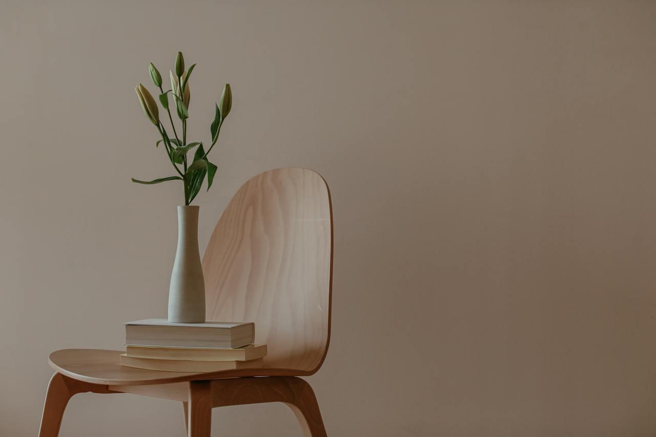White vase and books on a wooden chair.
