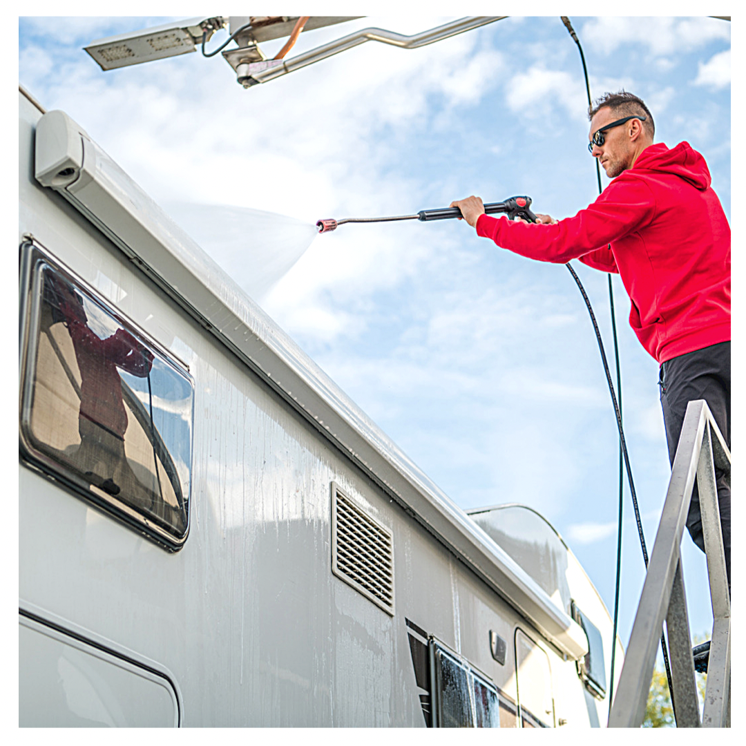 Man standing on ladder washing RV with hose.