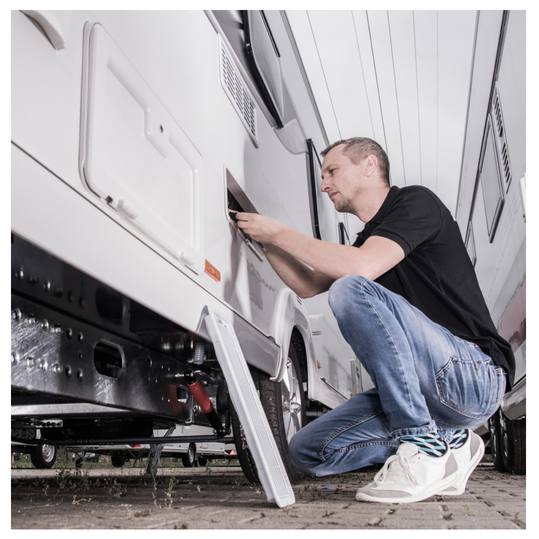 Man disconnecting something behind panel on exterior of RV.