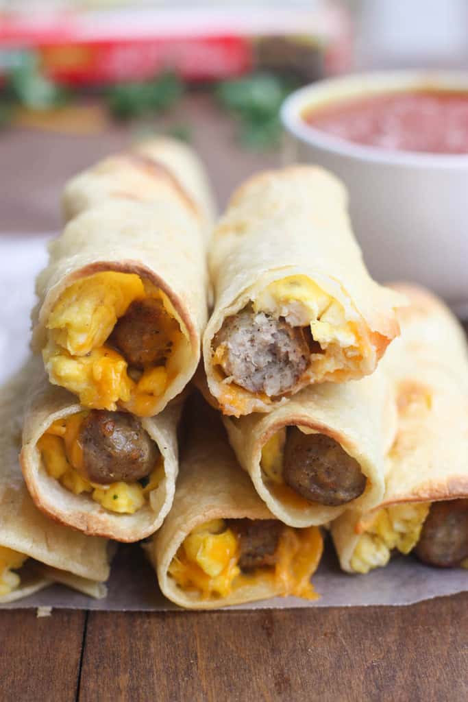 A stack of Egg and Sausage Breakfast Taquitos with salsa in the background.