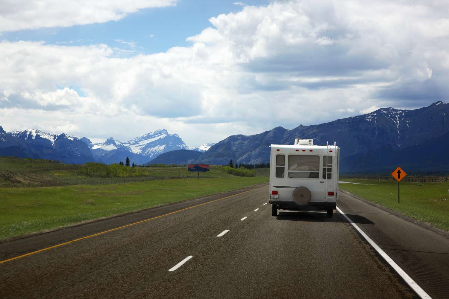 A picture of a travel trailer on an open highway with snow capped mountains in the background.